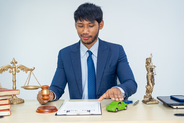 An Asian businessman in a formal suit works alone at a lawyer's desk, with golden scales, law...