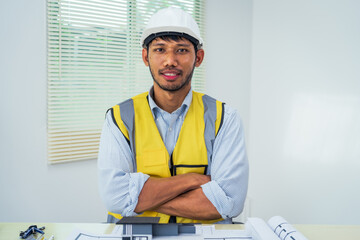 Asian architect works at a desk with house blueprints, checking plans on a laptop and clipboard,...