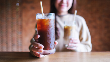 Closeup image of a young woman holding and serving two glasses of iced coffee