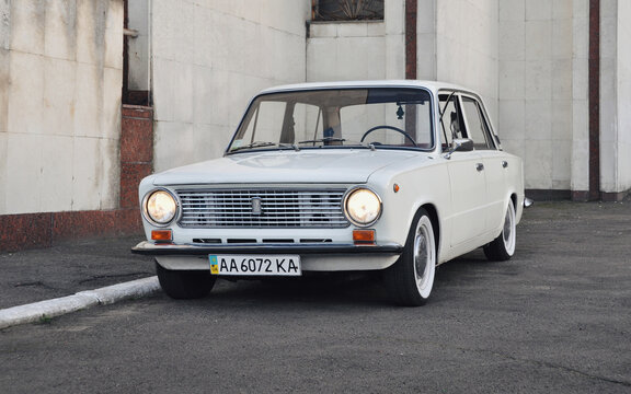 Old VAZ 2101 (aka Fiat 124) sedan parked near modernist building. White 1970s car with headlights turned on. Kyiv, Ukraine - September 08 2012.
