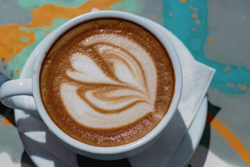 A white ceramic cup with fresh coffee and milk on a wooden table. The coffee forms a design on top, creating an inviting scene. Cup of aroma cappuccino coffee at a cafe with heart shape latte art