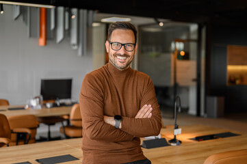 Portrait of handsome freelancer with eyeglasses and arms crossed smiling and standing in meeting room