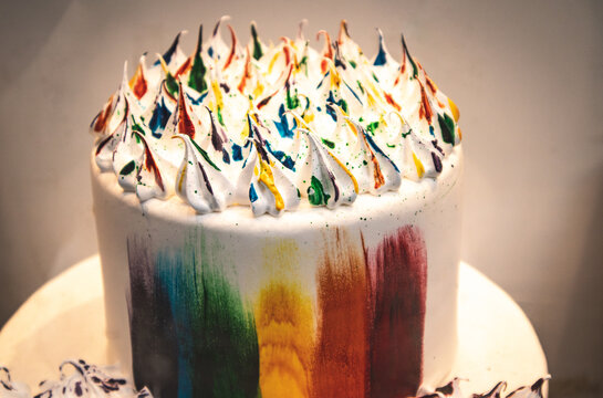 White cake painted with multicolored rainbow strokes. Confectionery in a store window. LGBT Pride month. Sweet dessert for gay party celebration.