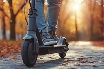 Obraz premium Close-up of a person riding an electric scooter on a city path with autumn leaves and sunset