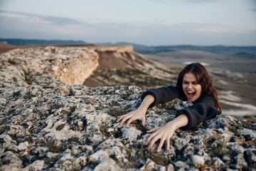 Young woman climbing a rock with outstretched arms under the bright daylight