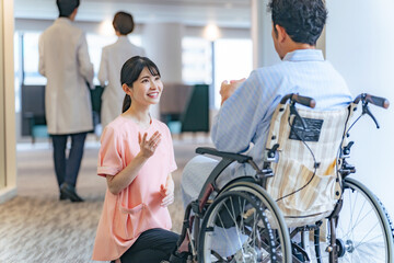 病院で車椅子の患者と会話する看護師