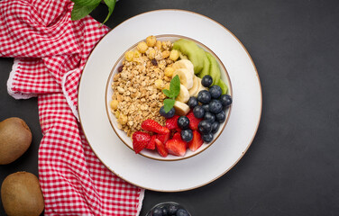 Granola with strawberries, kiwi, banana and blueberries in a round plate on a black table. Healthy and tasty food
