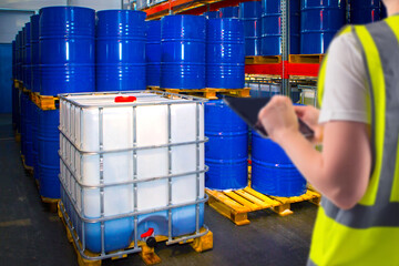 Chemical warehouse. Woman storekeeper with e-tablet. Toxic products are stored in barrels....