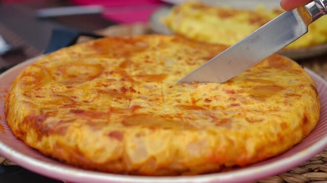 Man Cutting Homemade Spanish omelette (tortilla de patatas) with a knife at the center of a Spanish family&rsquo;s table