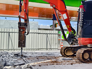 Excavator using hydraulic hammer for breaking concrete at a construction site