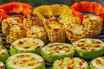 Vegetables are fried on a barbecue. Sliced zucchini pieces, corn and peppers. Vegetarian food