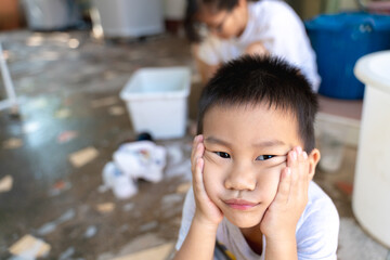 Bored Thai boy resting his face while his mother washes his shool shoes behind him.