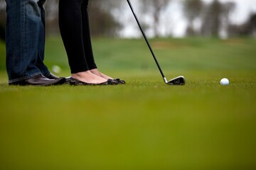 Couple standing close on golf course, focusing on putting a golf ball