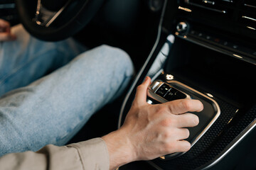 Closeup high-angle view of unrecognizable male sitting on driver seat shifting automatic transmission in car. Close-up hand of driver man moving lever arm on gearbox to add speed.