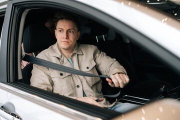 Portrait of handsome young man sitting on front passenger seat fastening belt harness. Closeup of passenger male with buckled security belt in car. Concept of safety lifestyle.