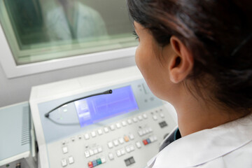 Audiologist woman doing the hearing exam to a mixed race man patient using an audiometer in a...