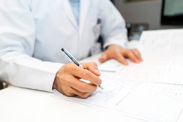 cardiologist looking at electrocardiograph ekg paper filling patient form. sitting and writing notes at the desk in clinic or hospital Office