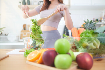 Beautiful young woman preparing a healthy vegetables salad in a kitchen with fresh ingredients. Healthy lifestyle, nutrition and dieting concept.
