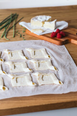 Preparing puff pastries squares with camembert cheese and fresh Raspberries on a wooden table.