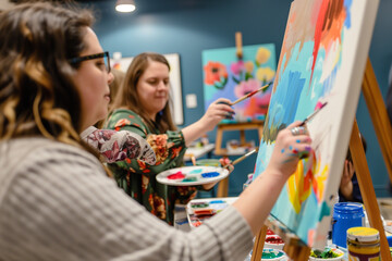 Friends attending an art class, each focused on their canvas with paint palettes and brushes in hand, colorful artwork in progress