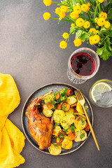 A hearty delicious dinner, baked rabbit with potatoes and carrots, a set table with food, a glass of wine and a vase of flowers