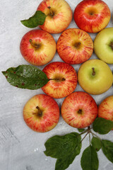 Fresh red and yellow apples with leaves on grey background, top view