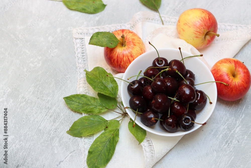 Wall mural Red apples and cherries in a plate on a light background with copy space. Summer fruit close up photo. Eating fresh concept. Ripe red apples and cherries in a bowl on a light background. 