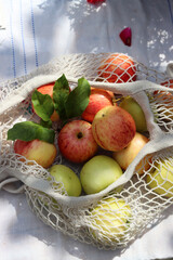 Green and red apples with leaves in white cotton mech bag. Eco friendly reusable shopping bag close up photo. Ripe apples in a string bag on a white tablecloth. Eating healthy concept. 