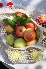 Green and red apples with leaves in white cotton mech bag. Eco friendly reusable shopping bag close up photo. Ripe apples in a string bag on a white tablecloth. Eating healthy concept. 