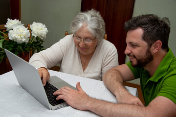 Elderly senior woman learning to use a laptop computer from teen male grandson