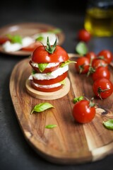 Stacked caprese salad with tomato, mozzarella cheese, and basil leaves on wooden board
