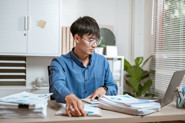 businessperson, document, executive, expertise, job, manager, occupation, paperwork, stress, working. A man is sitting with a pile of papers. He is looking at the papers and to be in a focused.