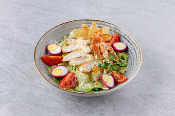 Caesar salad with chicken and bacon on a gray background on a plate for a restaurant menu