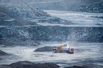 Loader filling a dump truck in diabase quarry with rocky terrain. Parekklisia quarry, Cyprus