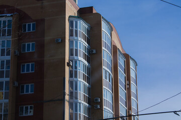 Modern apartment building with windows and balconies on blue sky background.