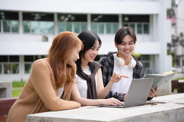 Three young adults happily collaborating on a school project outdoors, using a laptop and a...