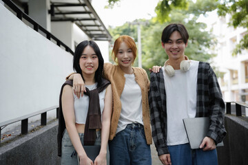 Three asian students are posing on a campus staircase with books and a laptop, prepared for a day of learning and camaraderie