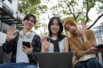 Three happy young individuals waving and smiling during a video chat on a laptop. Embracing virtual communication through technology