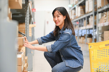Woman squatting and selecting a box from a shelf in a warehouse, smiling and focused.