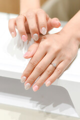 Hands with a glittery manicure resting on a UV lamp, showing off the finished nails with a touch of sparkle and elegance.