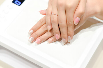 Hands with a glittery manicure resting on a UV lamp, showing off the finished nails with a touch of sparkle and elegance.