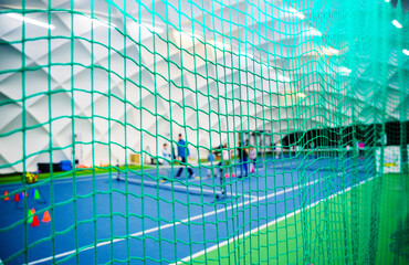 Obraz premium Tennis players practicing on indoor court behind green net. View of tennis players practicing on an indoor court, seen through a green net. The court has a blue and green surface and is inside a dome 