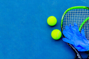 Top view of tennis rackets, balls, and blue protective gloves on a blue tennis court. The empty...