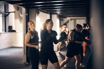 Young female coach laughing with a woman wearing boxing gloves doing a punching workout during a boxing class at the gym