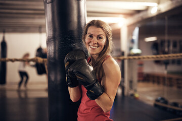 Smiling woman standing by a punching bag in a boxing gym