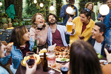 Exuberant friends enjoying outdoor feast with wine and beer, laughter-filled garden party under...