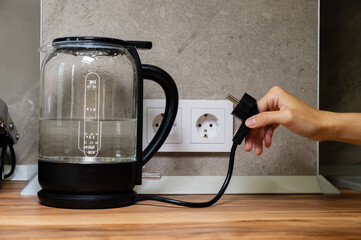 Woman connecting an electric kettle to a socket indoors, close-up