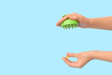 Female hand with silicone head massage brush and hair vitamin capsule on blue background