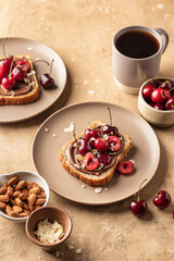 Breakfast toast with chocolate paste, sweet cherry and almond petals on beige textured background close up. Breakfast for kids