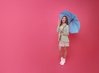 Happy smile Asian woman standing and holding blue umbrella and pointing finger isolated on pink background, life insurance and protection concept.